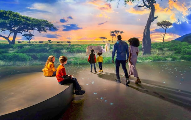 Visitors at Illuminarium Las Vegas experience a virtual safari landscape.