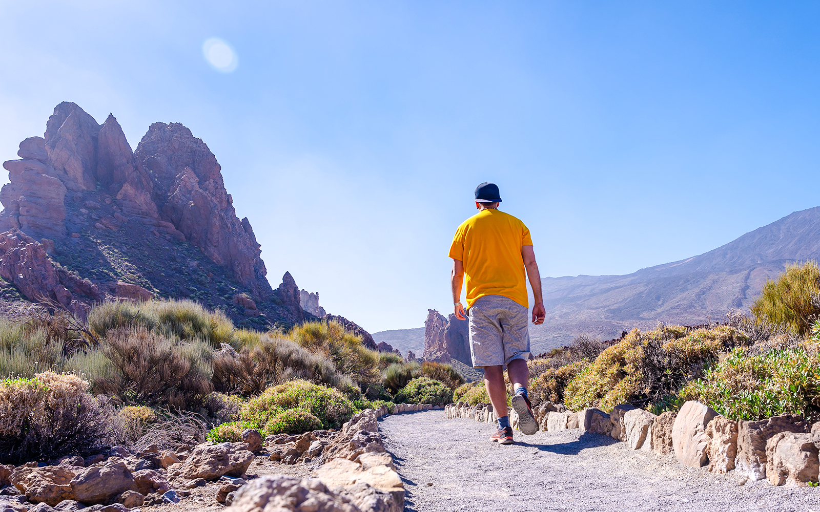 Man walking on a trail in Teide National Park, Tenerife, with rocky mountains in the background.