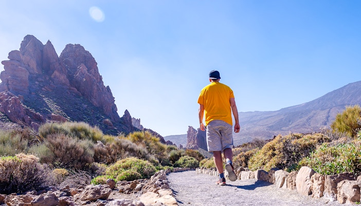 Man walking on a trail in Teide National Park, Tenerife, with rocky mountains in the background.