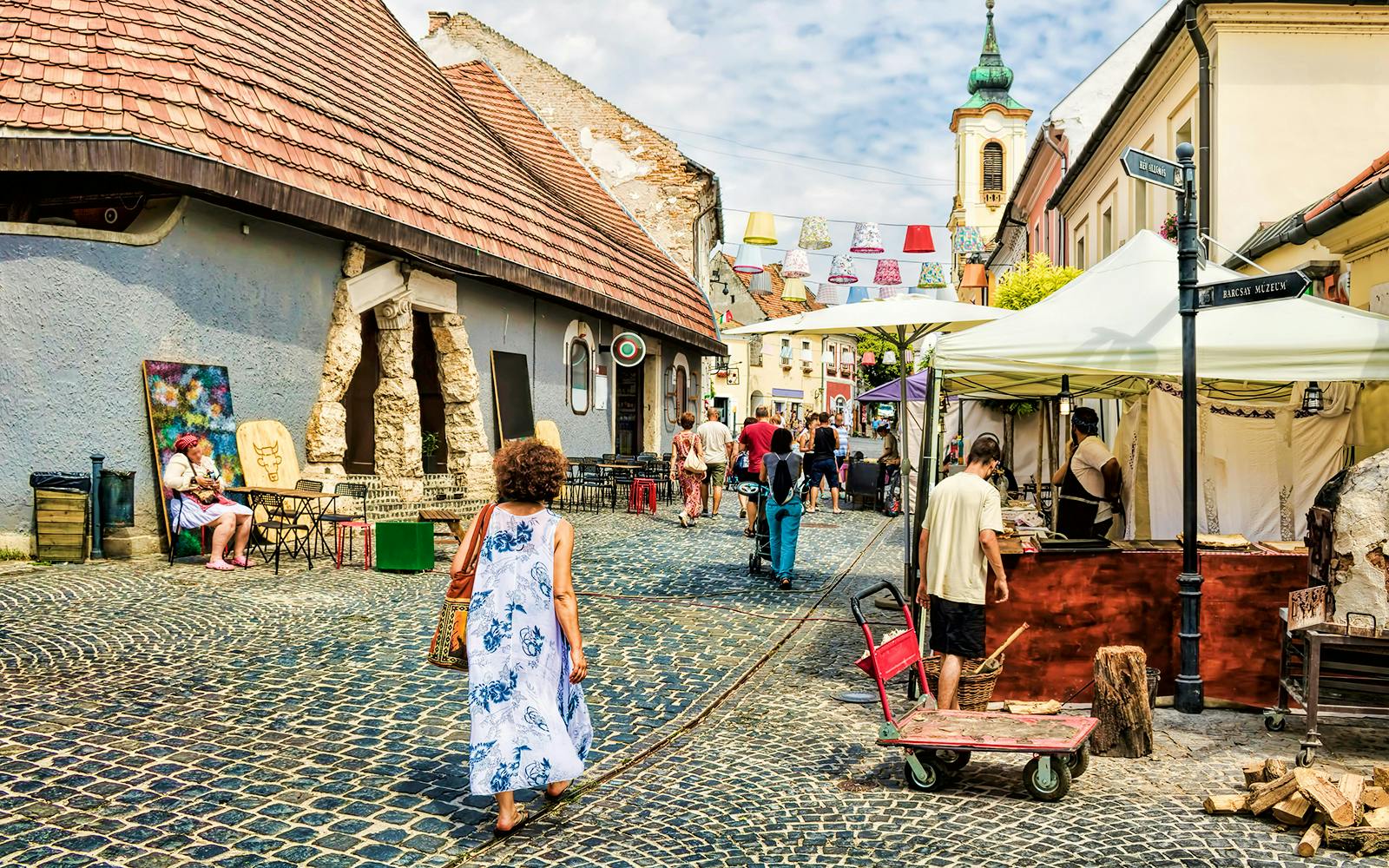 Guests walking through cobblestone streets in Szentendre, Hungary, near local shops and market stalls.