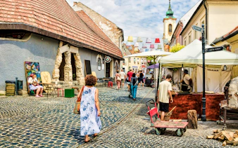 Guests walking through cobblestone streets in Szentendre, Hungary, near local shops and market stalls.