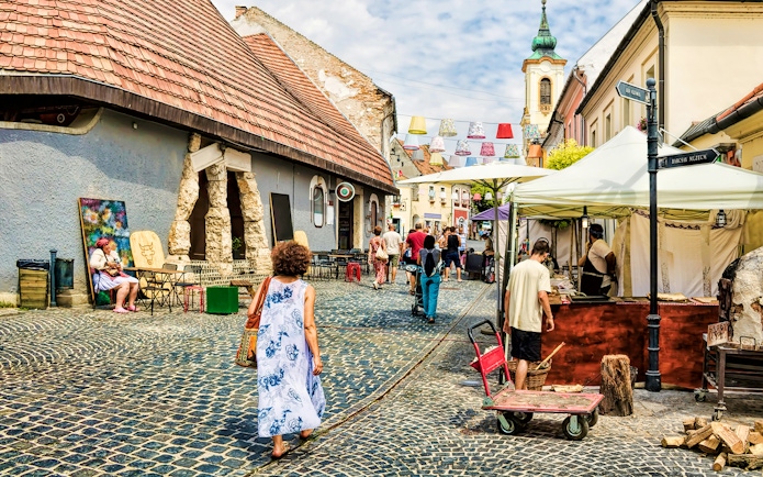 Guests walking through cobblestone streets in Szentendre, Hungary, near local shops and market stalls.