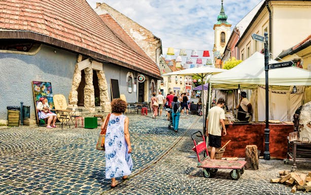 Guests walking through cobblestone streets in Szentendre, Hungary, near local shops and market stalls.