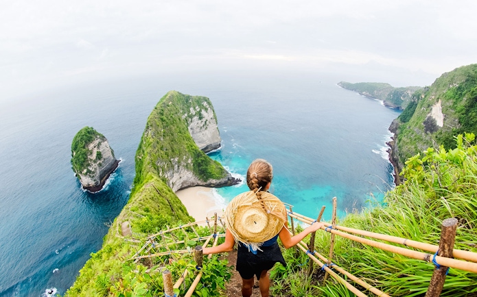 Traveler overlooking Kelingking Beach cliffs on Nusa Penida Island, Bali.