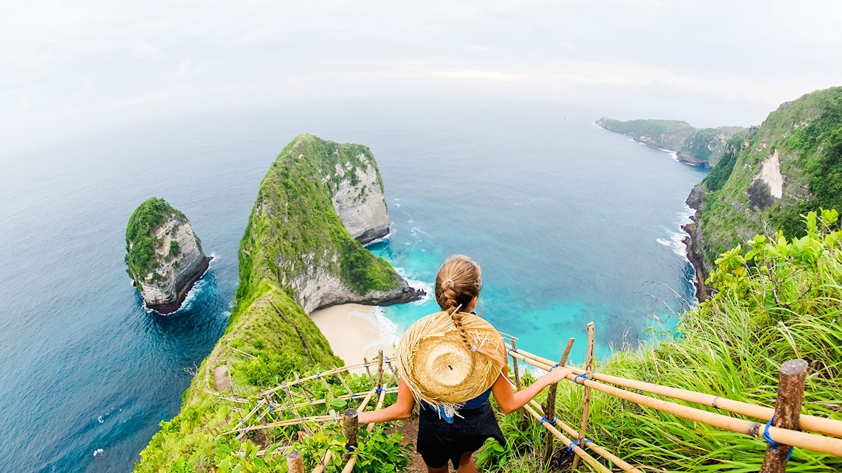 Traveler overlooking Kelingking Beach cliffs on Nusa Penida Island, Bali.
