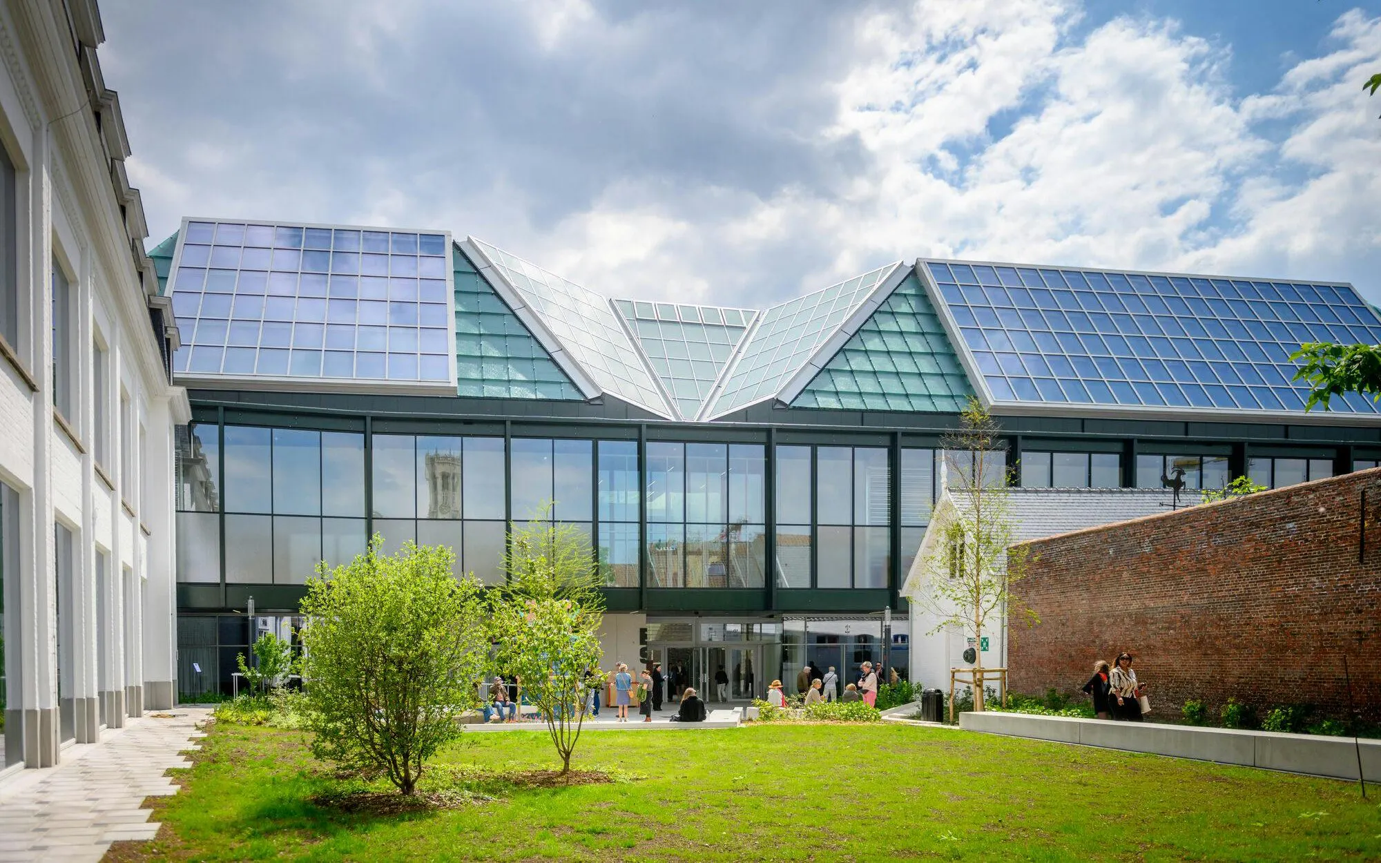 Modern building with glass facade and solar panels at BRUSK, people gathered outside.