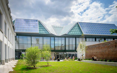 Modern building with glass facade and solar panels at BRUSK, people gathered outside.