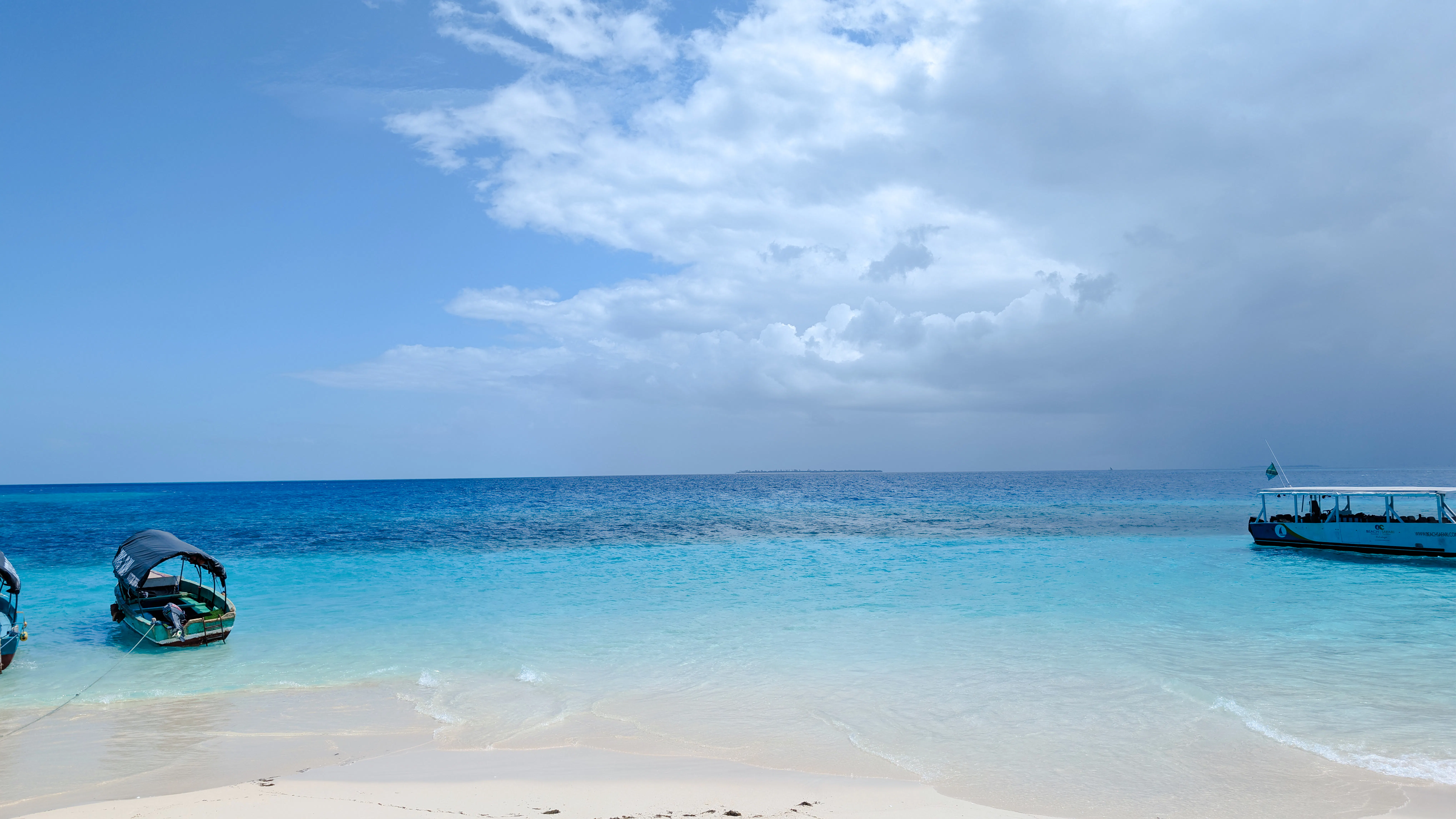 Boats anchored near a sandy beach with clear blue water in Zanzibar.