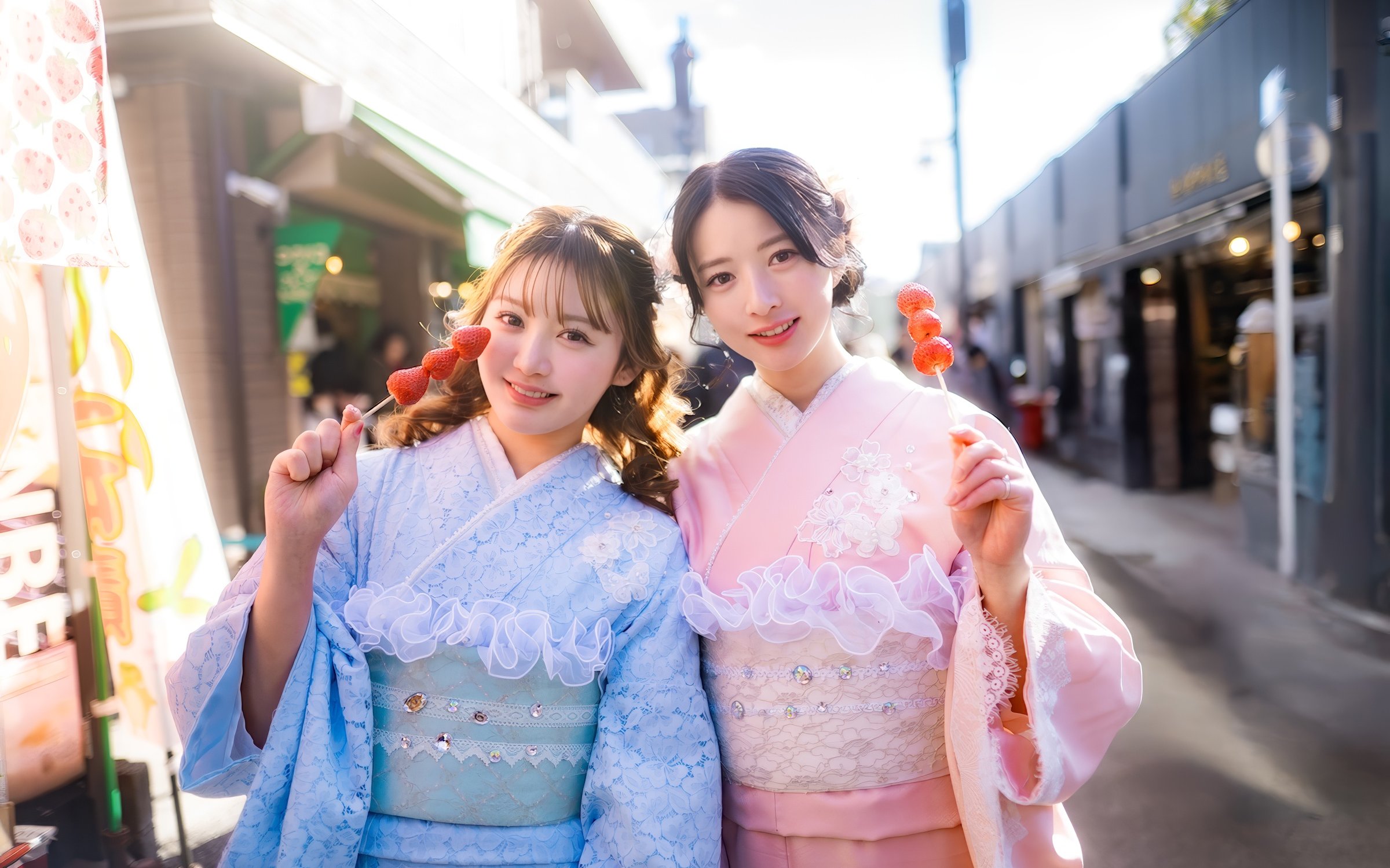Friends in kimonos holding strawberry skewers on a street in Japan.