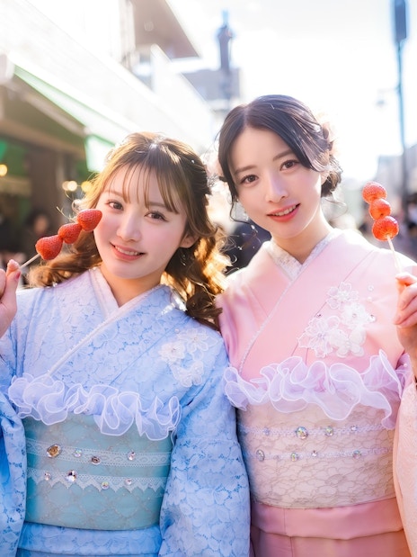 Friends in kimonos holding strawberry skewers on a street in Japan.