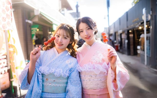 Friends in kimonos holding strawberry skewers on a street in Japan.