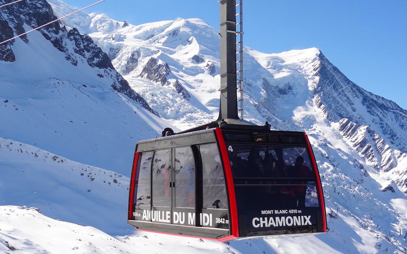 Cable car ascending Mont Blanc in Chamonix with snowy peaks in the background.