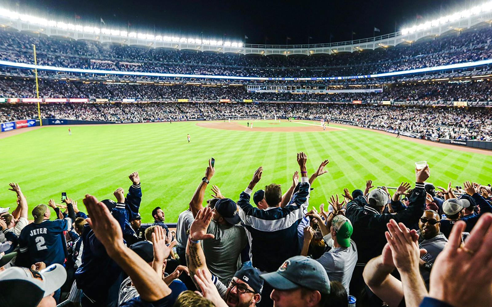 Fans cheering at a Yankees game in a packed stadium at night.