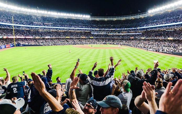 Fans cheering at a Yankees game in a packed stadium at night.