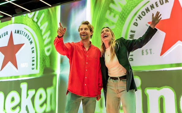 Tourists smiling and pointing at Heineken Experience in Amsterdam.
