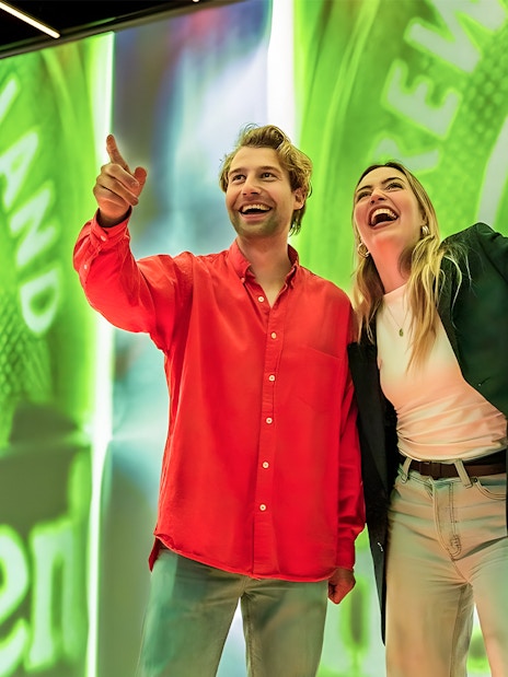 Tourists smiling and pointing at Heineken Experience in Amsterdam.