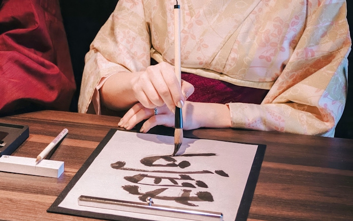 Kimono-clad person practicing Japanese calligraphy at a tea ceremony.