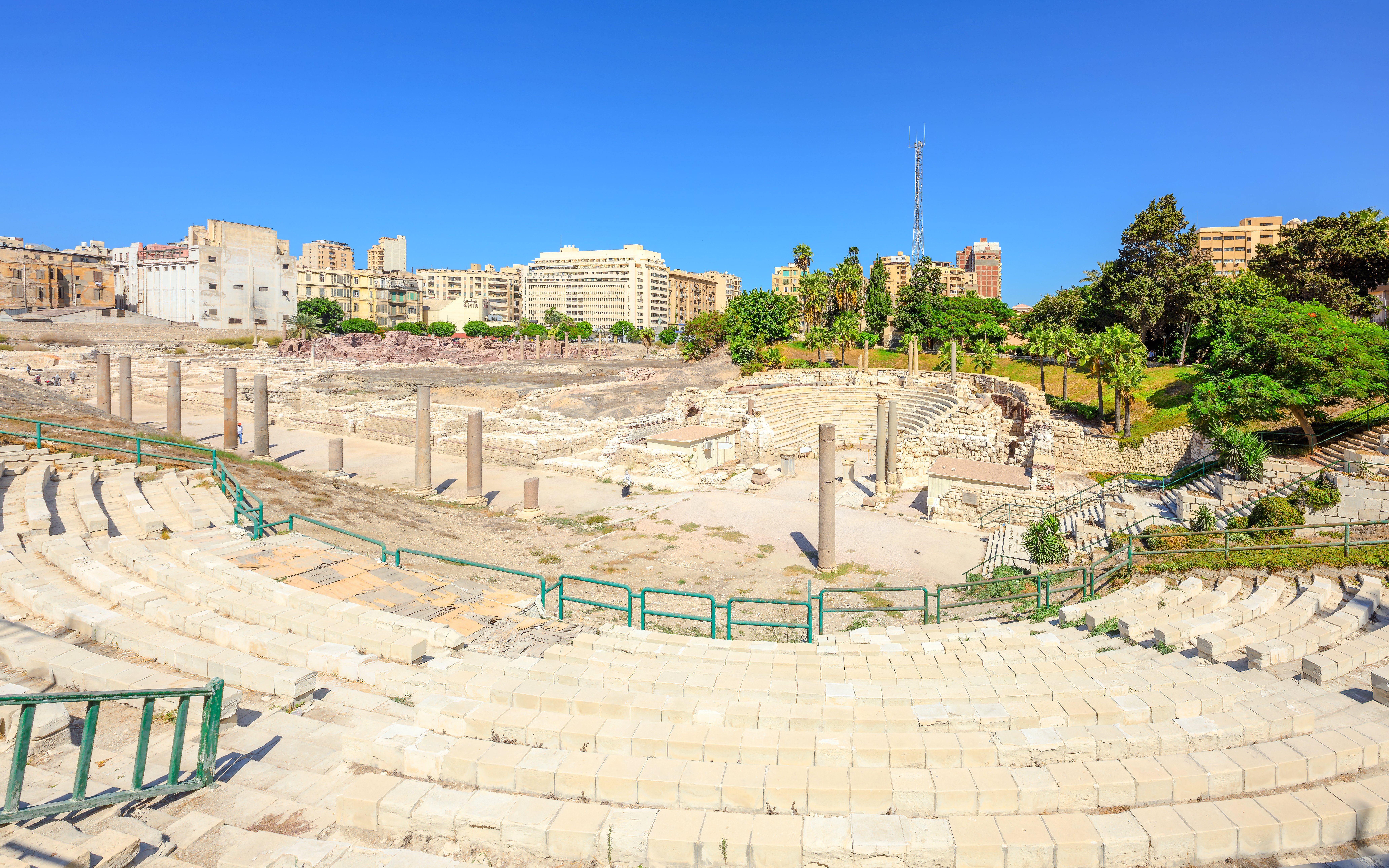 Ancient Roman Theatre ruins in Kom El-Deka, Alexandria, with surrounding cityscape.