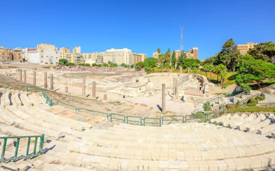 Ancient Roman Theatre ruins in Kom El-Deka, Alexandria, with surrounding cityscape.