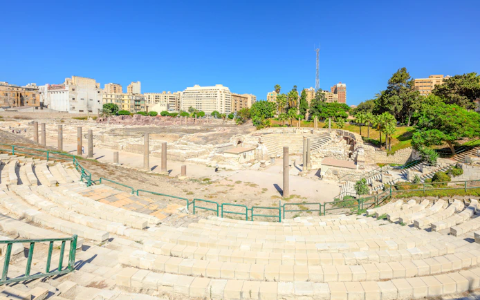 Ancient Roman Theatre ruins in Kom El-Deka, Alexandria, with surrounding cityscape.