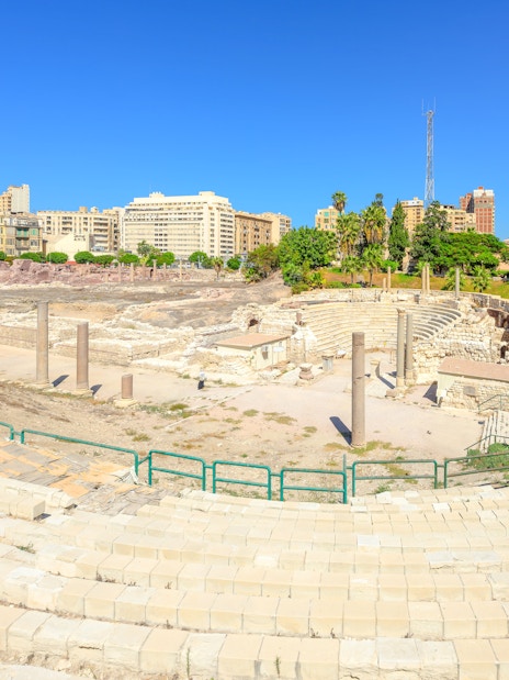 Ancient Roman Theatre ruins in Kom El-Deka, Alexandria, with surrounding cityscape.