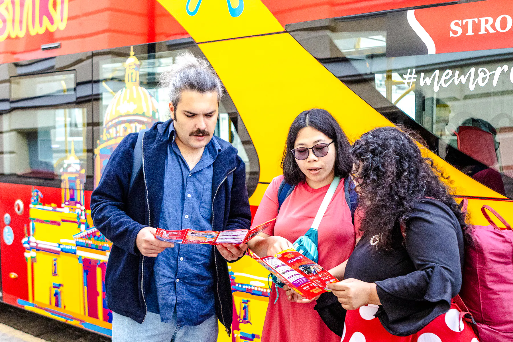 Tourists reading maps in front of a Helsinki Hop On-Hop Off bus.