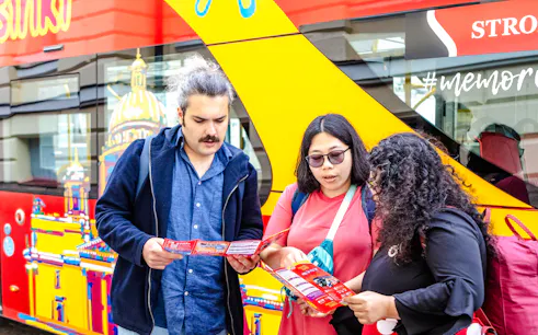 Tourists reading maps in front of a Helsinki Hop On-Hop Off bus.