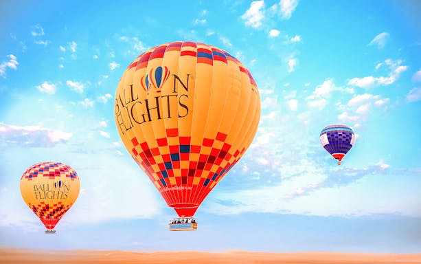 Hot air balloons floating over a desert landscape under a clear blue sky.