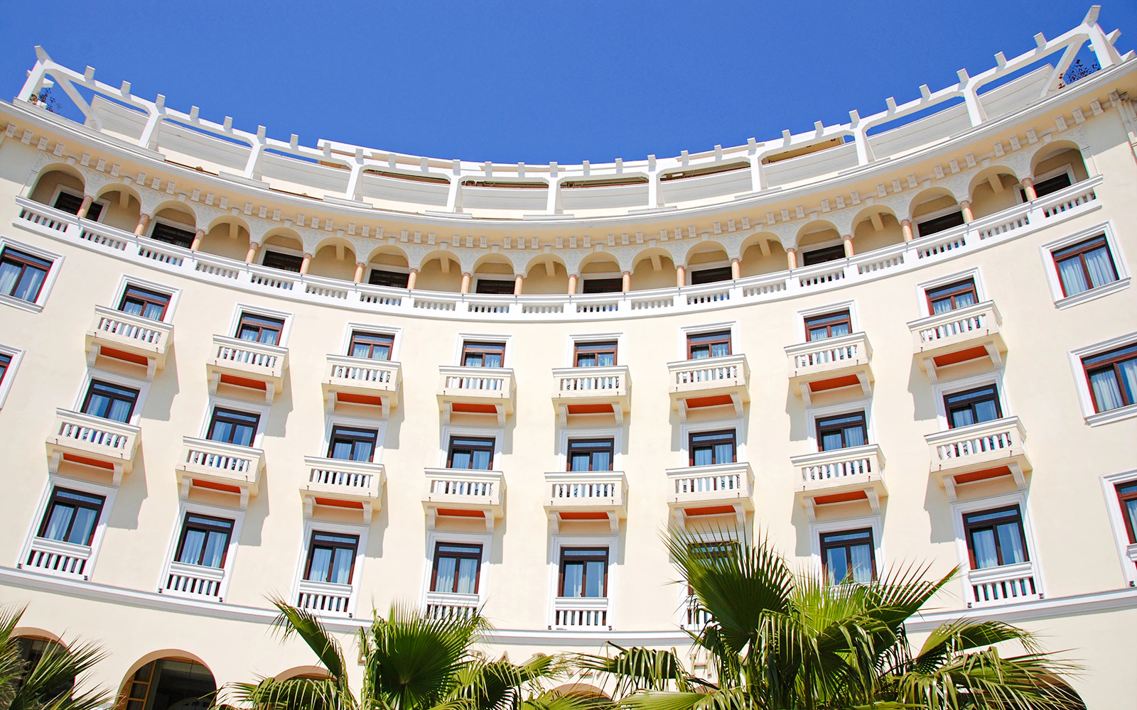 Luxurious hotel exterior with arched balconies and palm trees.