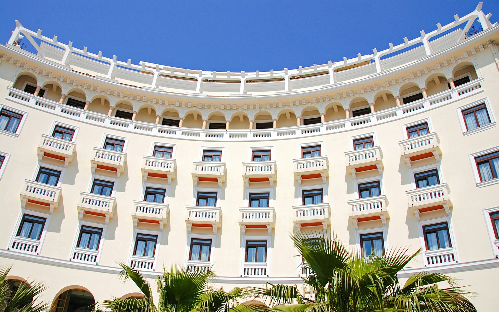 Luxurious hotel exterior with arched balconies and palm trees.