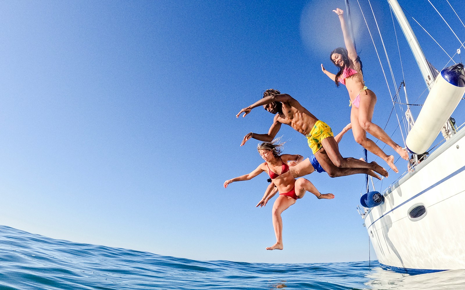 Friends jumping off a sailboat into the ocean.