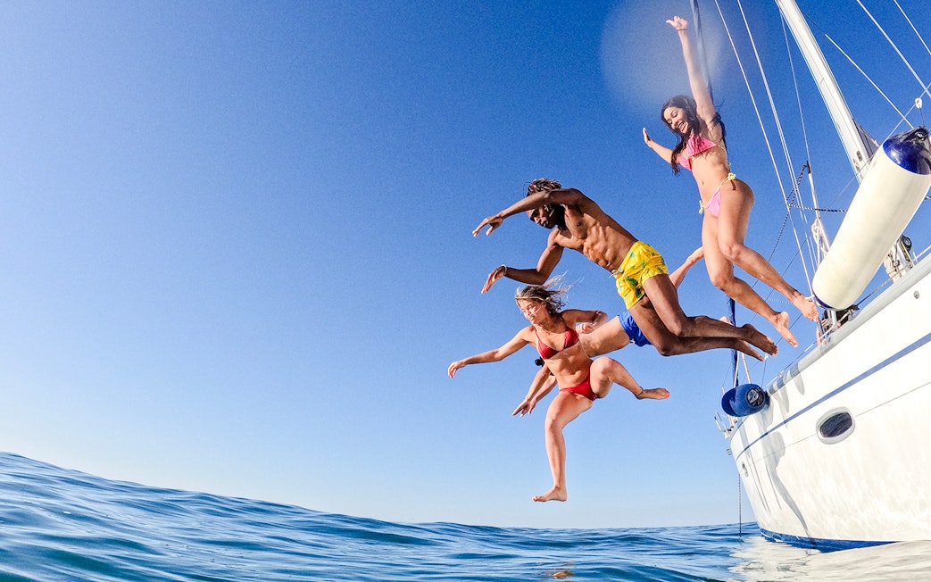 Friends jumping off a sailboat into the ocean.