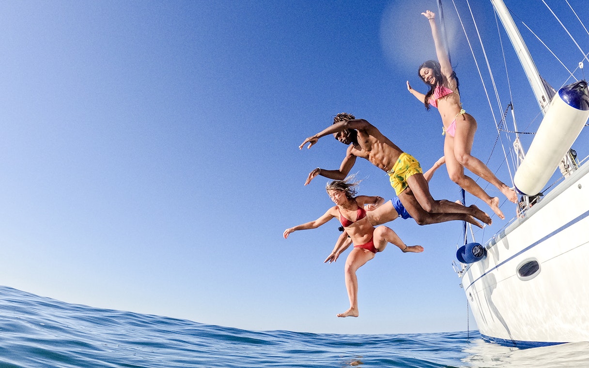 Friends jumping off a sailboat into the ocean.