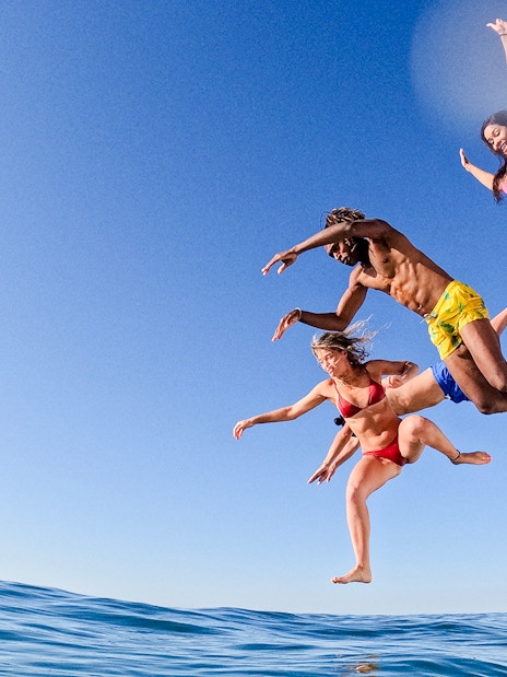 Friends jumping off a sailboat into the ocean.