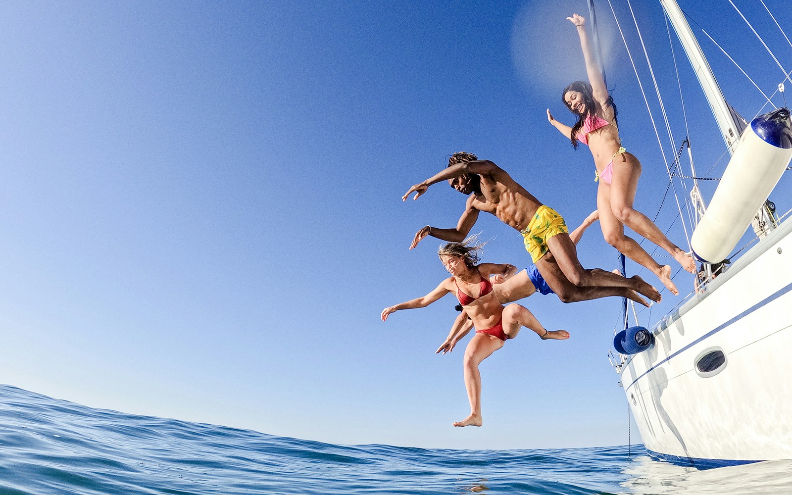 Friends jumping off a sailboat into the ocean.