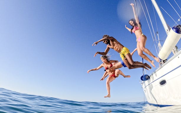 Friends jumping off a sailboat into the ocean.