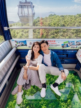 Couple enjoying view from crystal cabin cable car with glass floor over lush forest.