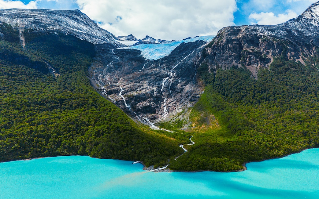 Balmaceda Glacier with turquoise lake in Patagonia, Chile, surrounded by lush forest and mountains.
