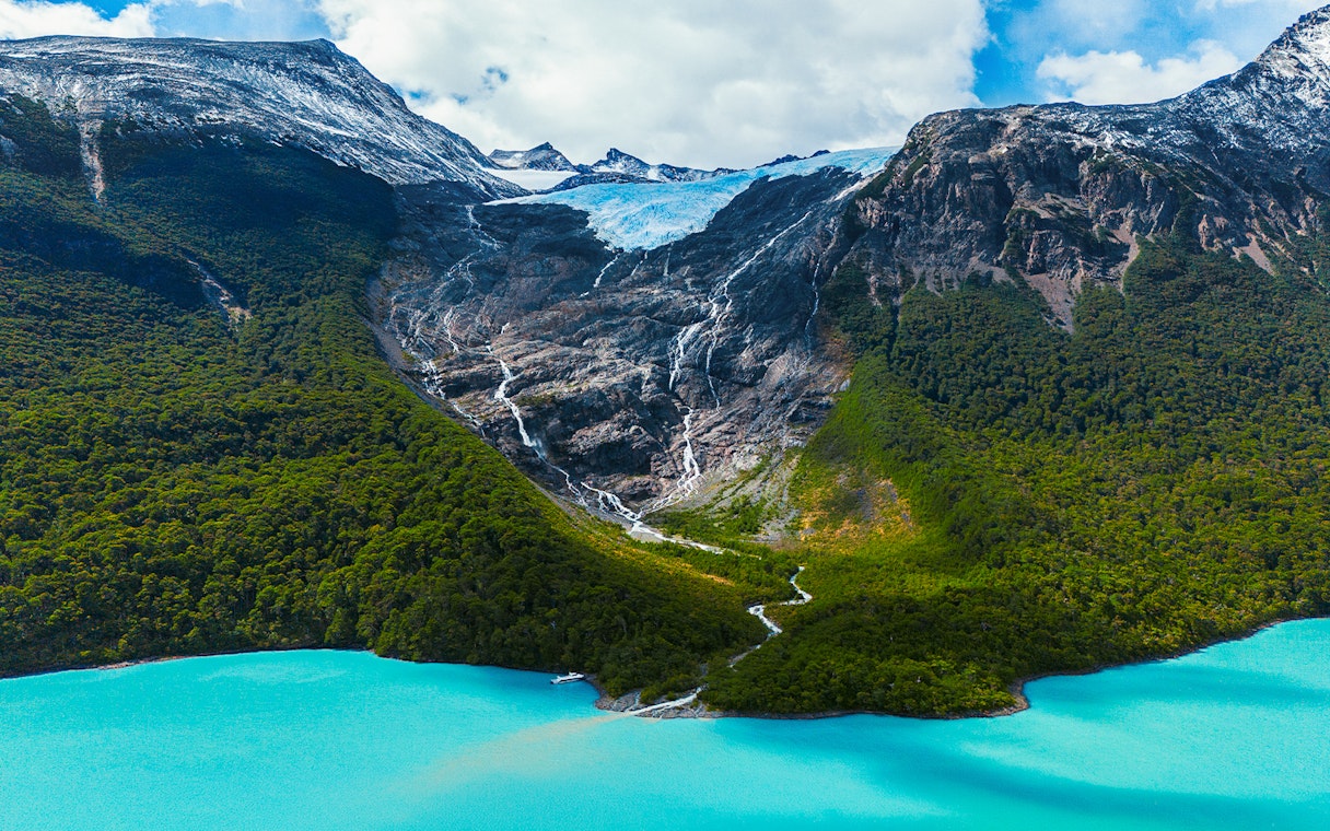 Balmaceda Glacier with turquoise lake in Patagonia, Chile, surrounded by lush forest and mountains.