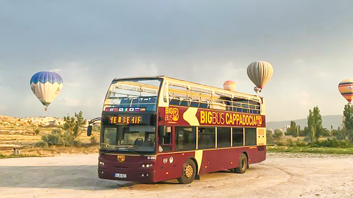 Cappadocia hop-on hop-off bus with hot air balloons in the background.