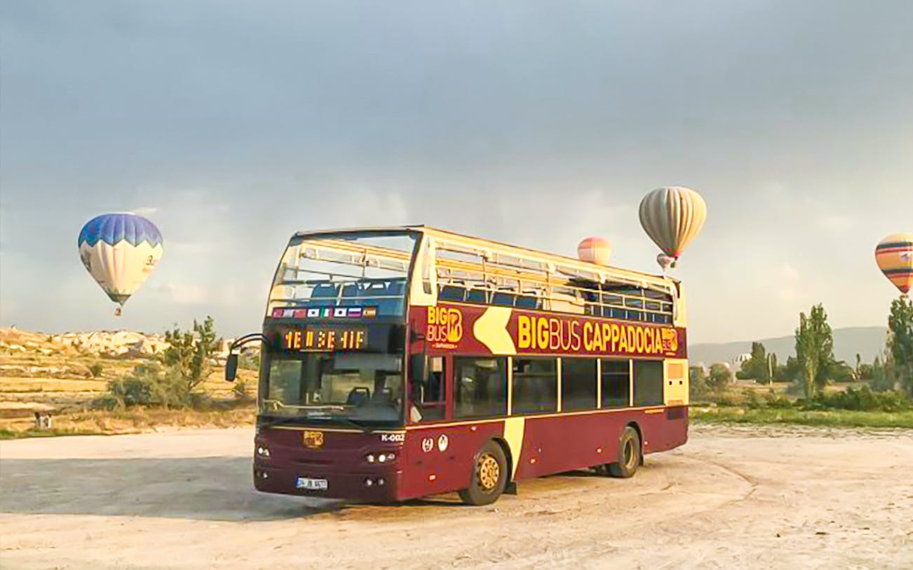 Cappadocia hop-on hop-off bus with hot air balloons in the background.