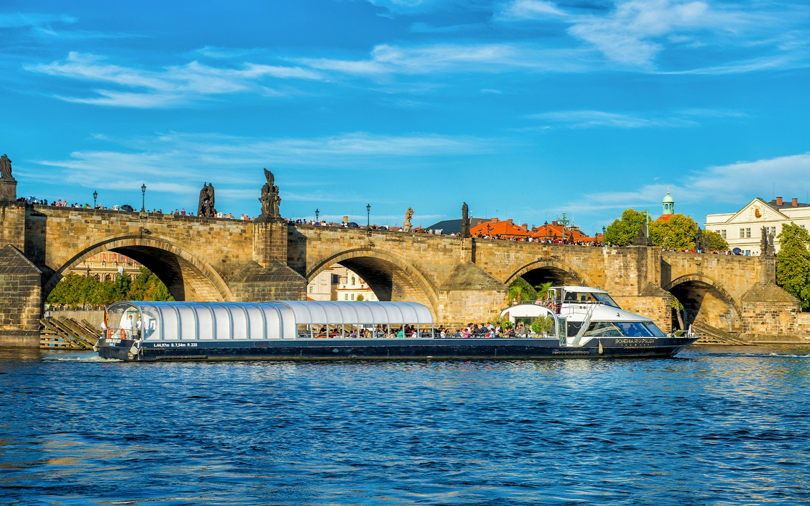 Vltava River cruise boat passing under Charles Bridge in Prague.