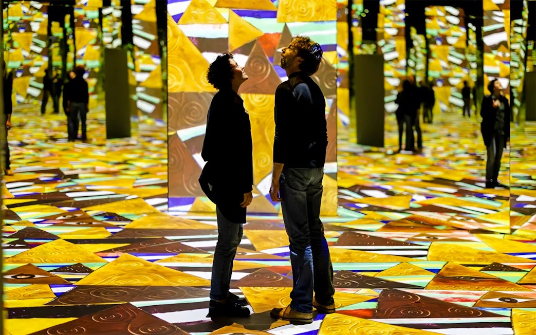 Visitors at Gustav Klimt Exhibit, Port des Lumières, Hamburg, surrounded by vibrant projections.