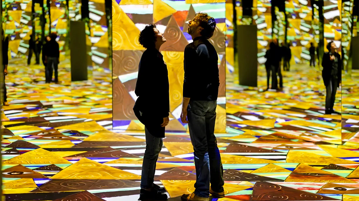 Visitors at Gustav Klimt Exhibit, Port des Lumières, Hamburg, surrounded by vibrant projections.