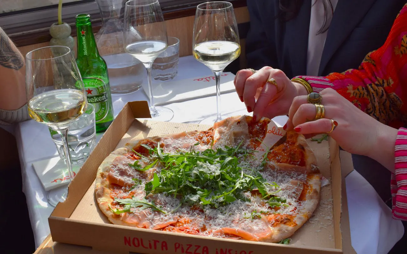 Freshly baked Nolita pizza on Haarlem canal dinner cruise table with wine glasses.