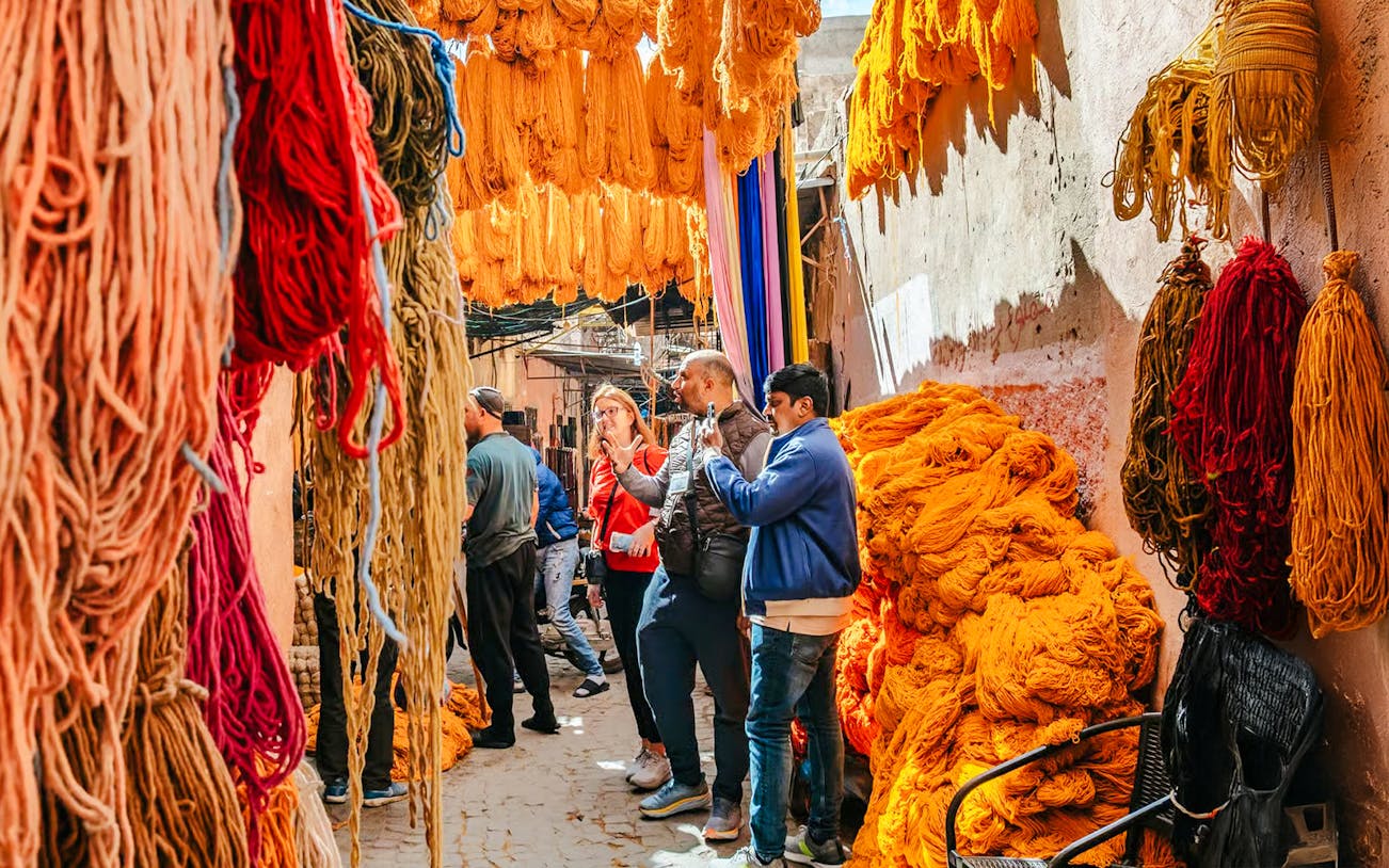 Visitors exploring vibrant yarn displays in Marrakech souks during a private shopping tour.