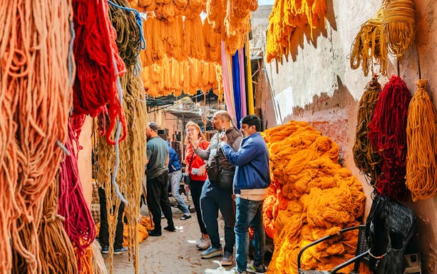 Visitors exploring vibrant yarn displays in Marrakech souks during a private shopping tour.
