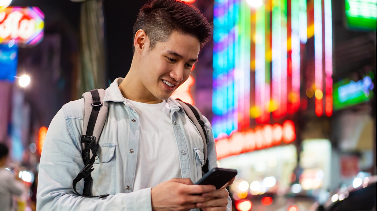 Man using smartphone on a vibrant city street at night.