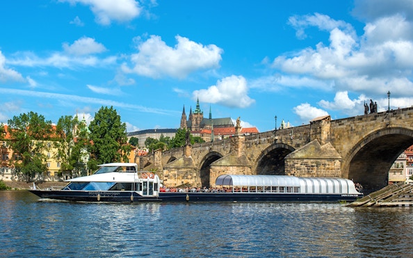 Vltava River cruise boat passing under Charles Bridge in Prague.