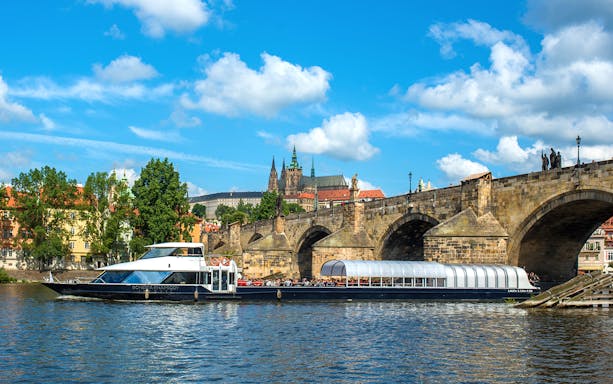 Vltava River cruise boat passing under Charles Bridge in Prague.